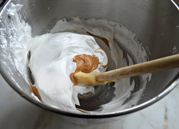 Spatula folding peanut butter into a egg and sugar mixture.