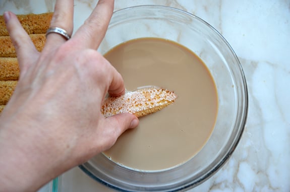 Person dipping a ladyfinger into an espresso mixture.