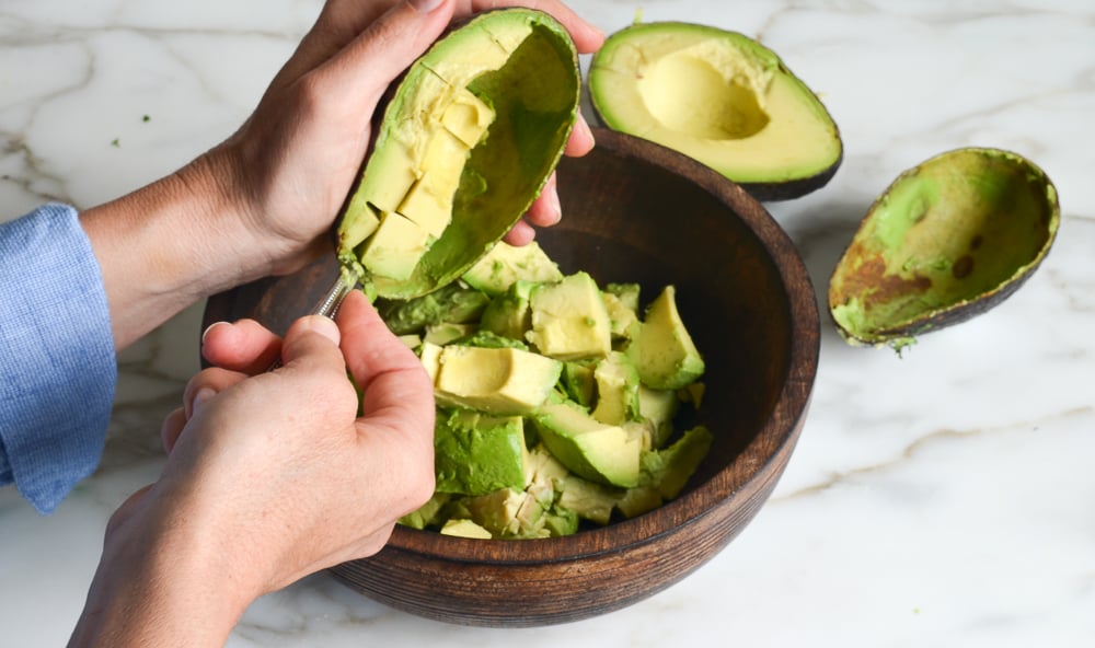 scooping avocado flesh into bowl