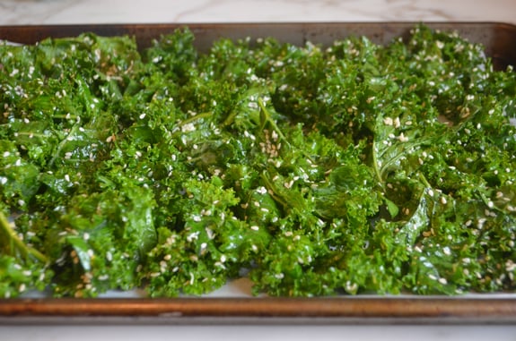 Seasoned kale on a lined baking sheet.