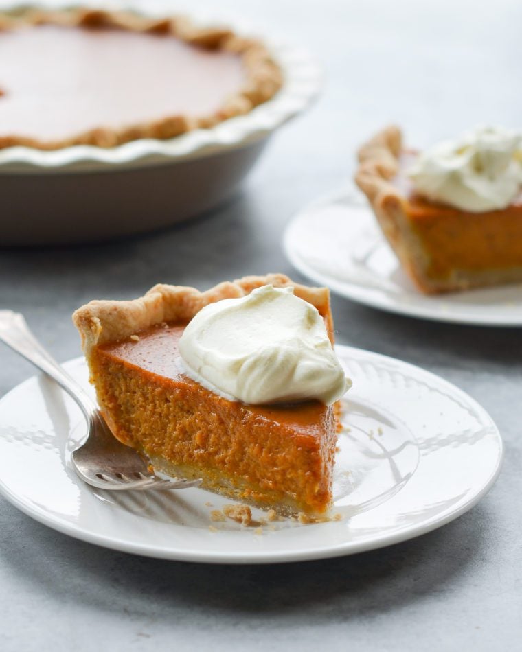 Slice of pumpkin pie on a plate with a fork.