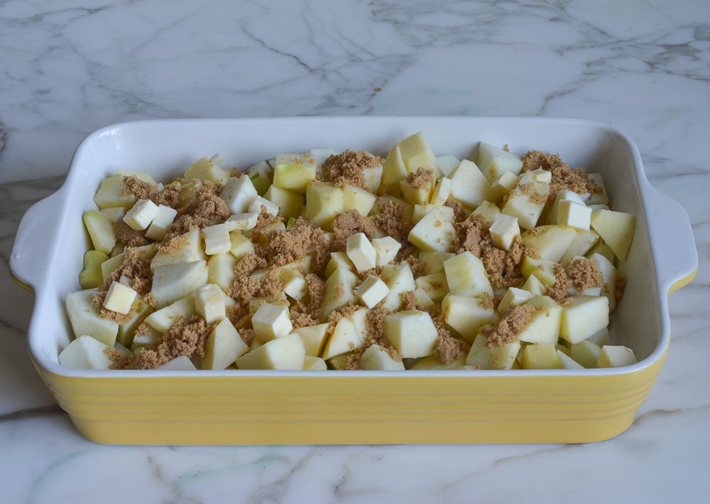 Apple chunks in a baking dish with brown sugar and butter.