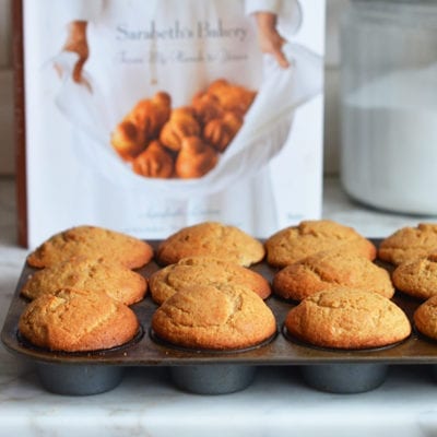 Muffin tin of maple muffins in front of a cookbook.