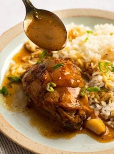 Spoon drizzling sauce over a plate of chicken and rice.