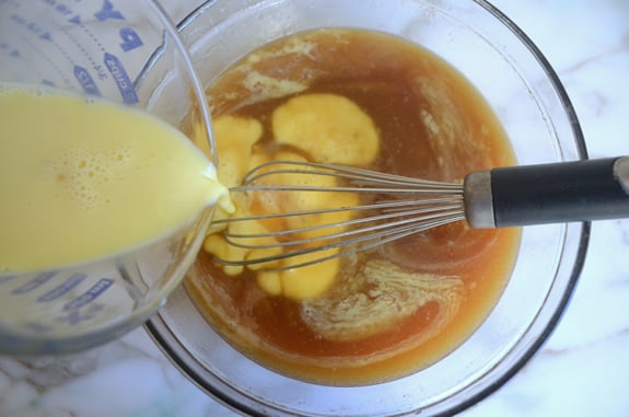 Eggs pouring into a bowl of syrup mixture.