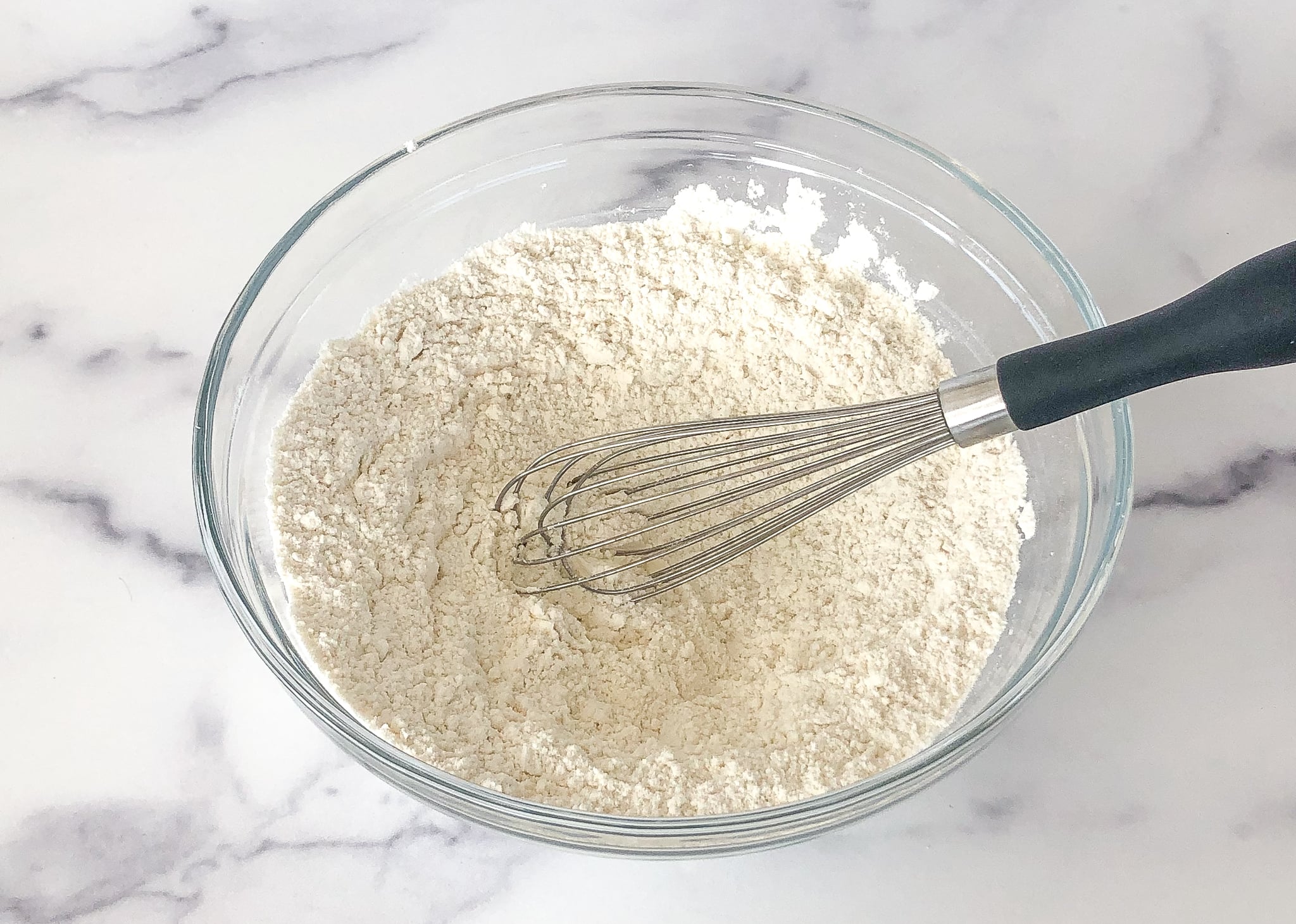 A bowl of flour with a whisk resting to the side.