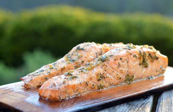 Cedar planked salmon with lemon, garlic, and herbs on a table.