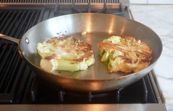 Browned cauliflower steaks in a pan.