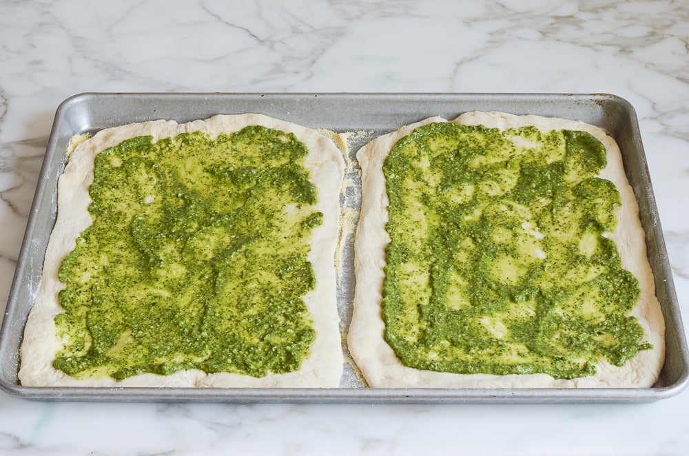 spreading pesto on pizza dough