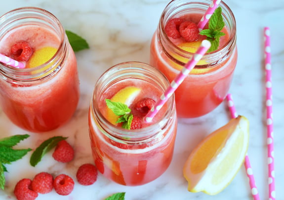 Three jars of raspberry lemonade with fruit and straws.
