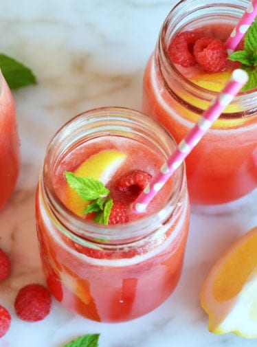 Jars of raspberry lemonade with fruit and straws.
