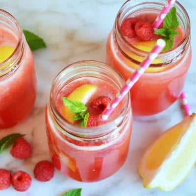 Jars of raspberry lemonade with fruit and straws.