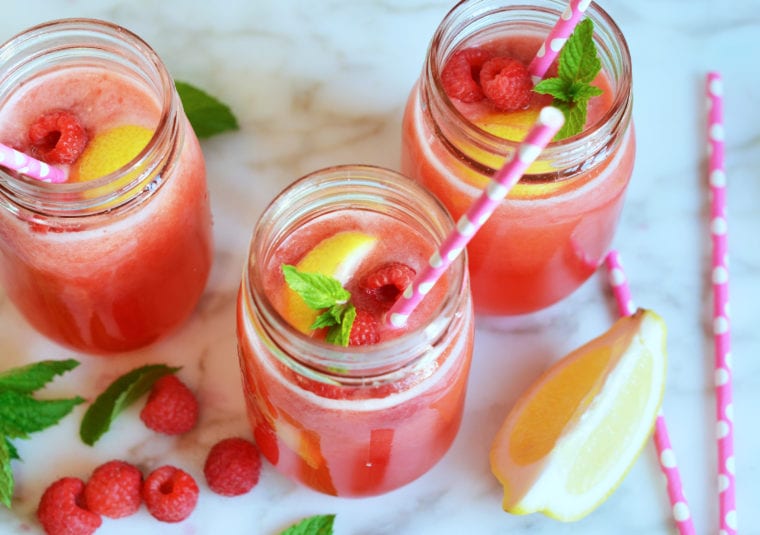 Jars of raspberry lemonade with fruit and straws.