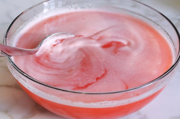 Spoon stirring a bowl of raspberry lemonade.