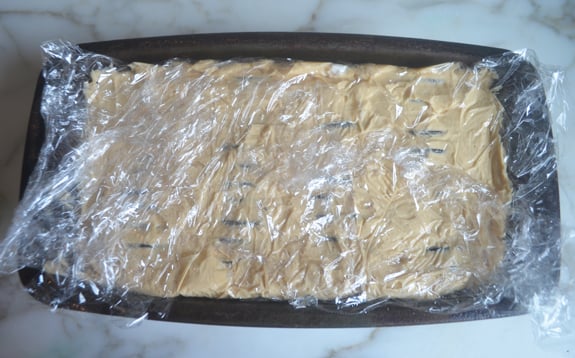 Cake wrapped in plastic wrap in a loaf pan.