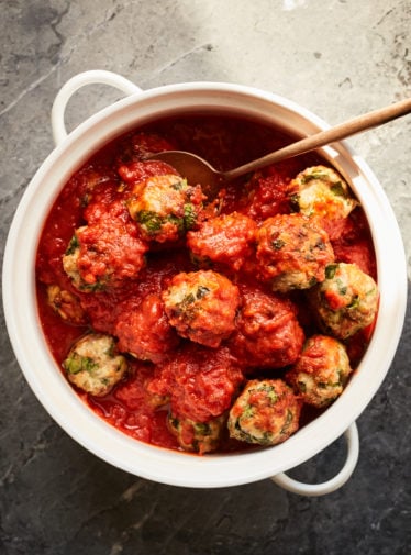Spoon grabbing a meatball from a dish.