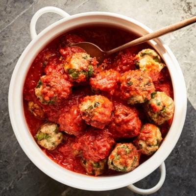 Spoon grabbing a meatball from a dish.