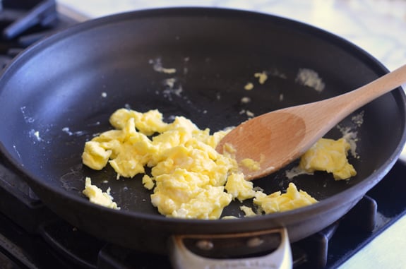Wooden spoon stirring a skillet of scrambled eggs.