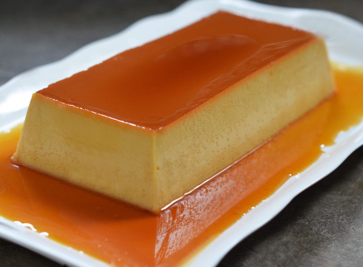 Mexican flan on a platter with caramel sauce pooling on the sides.