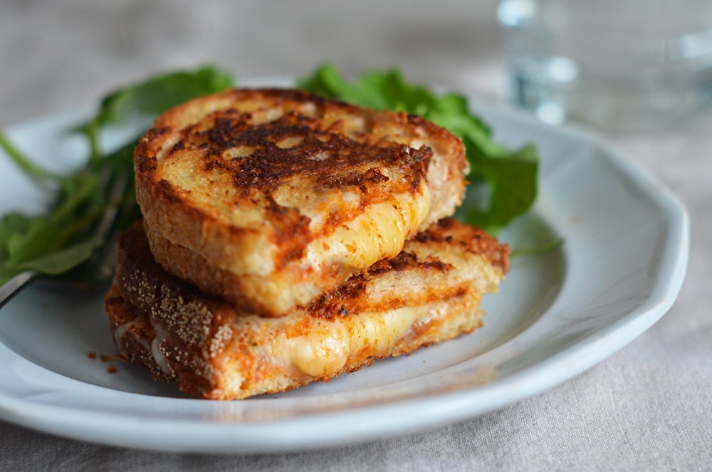 Halved grilled cheese sandwich with sun-dried tomato pesto stacked on a plate.