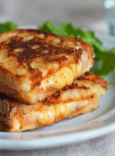 Halved grilled cheese sandwich stacked on a plate.