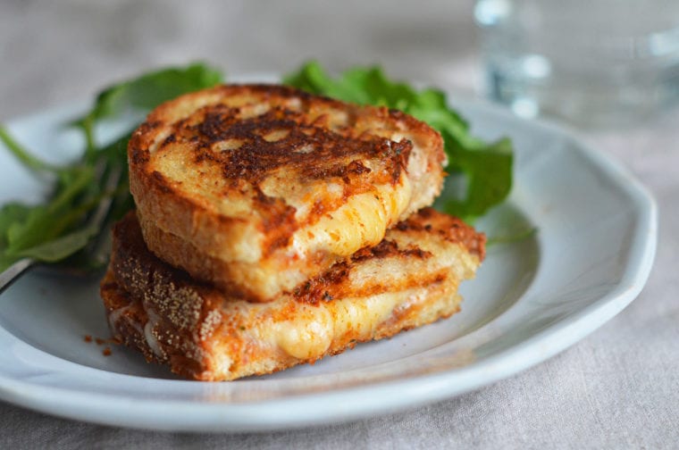 Halved grilled cheese sandwich stacked on a plate.