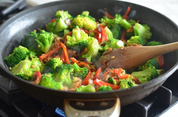 Broccoli in a skillet with seasonings and other vegetables.