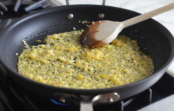 Wooden spoon stirring shallots and garlic in a skillet.