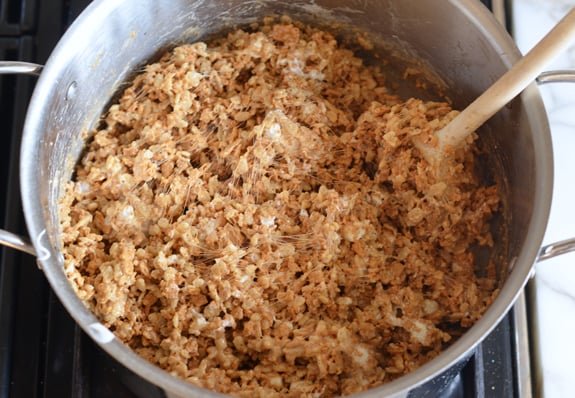 Wooden spoon stirring a sticky cereal mixture.