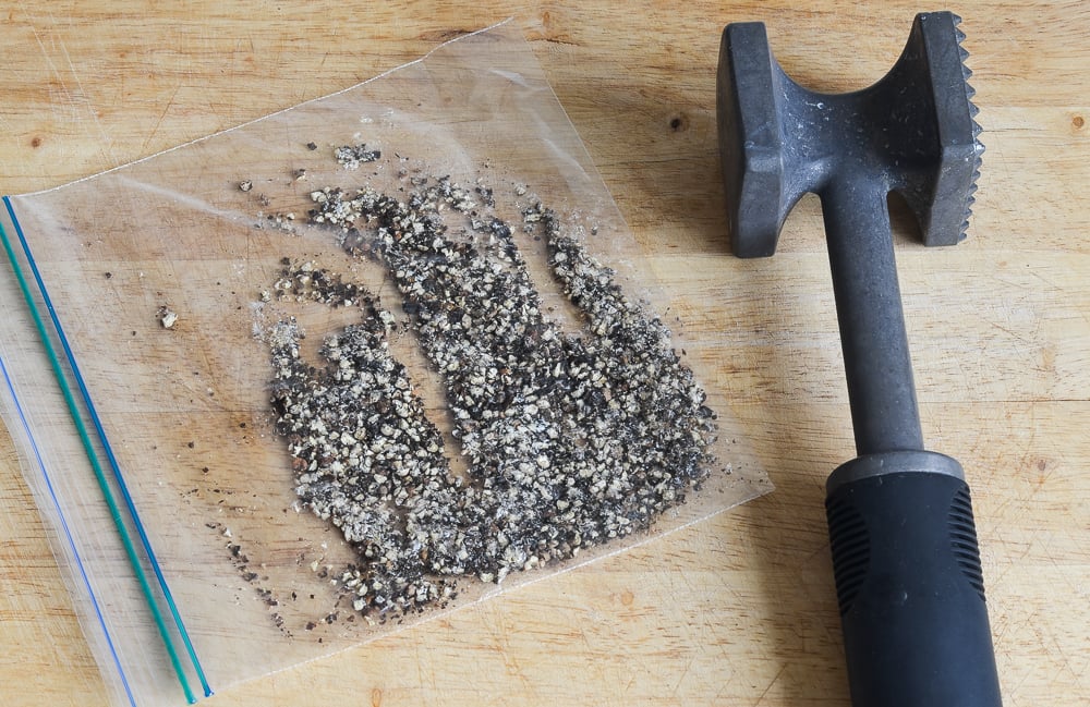 Pounding the peppercorns for steak au poivre with peppercorns in a bag and a mallet to the side.