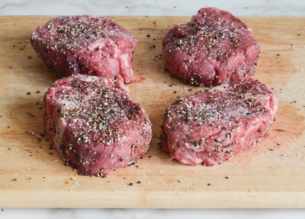 Seasoned steaks on a wooden cutting board.