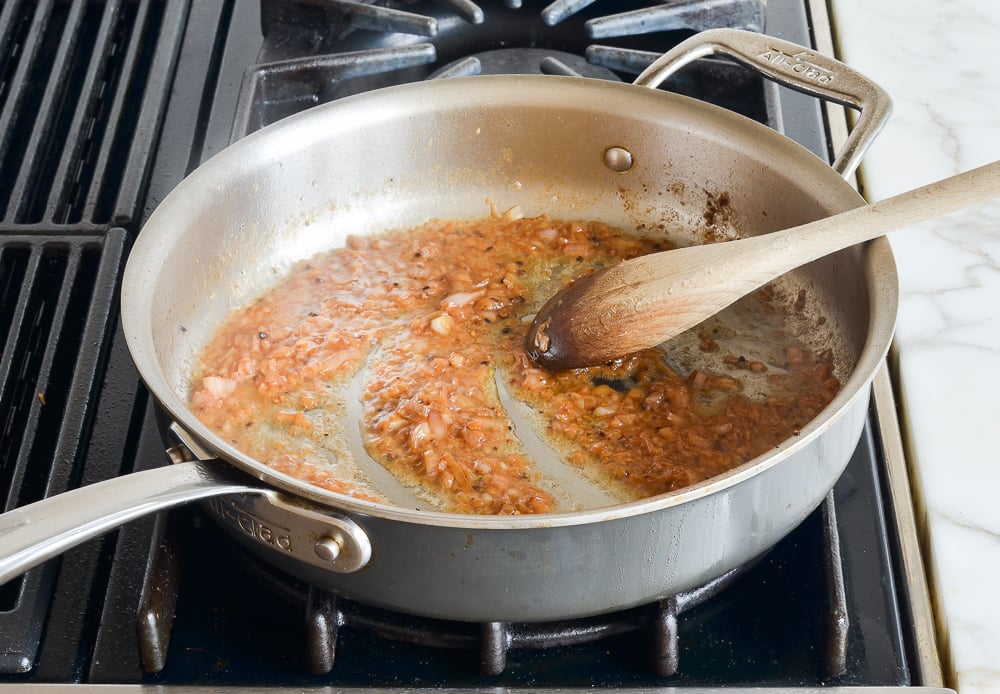 Cognac reduced to a glaze in a skillet with a wooden spoon resting to the side.