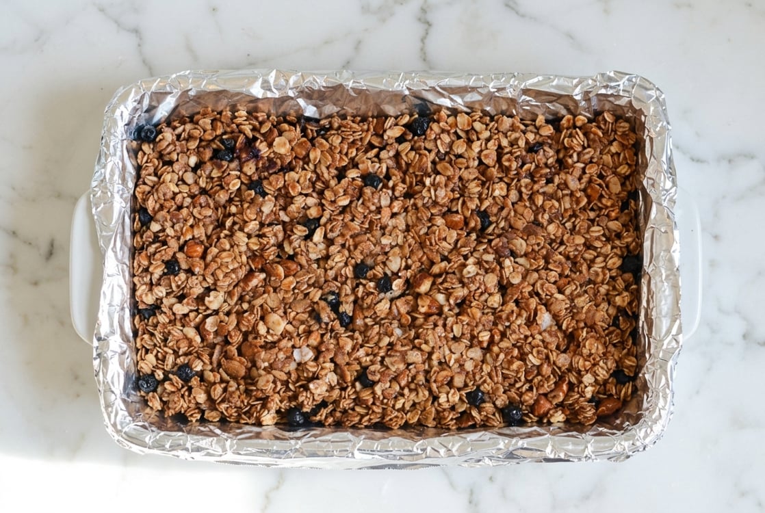 Blueberry granola bars pressed into foil-lined pan.