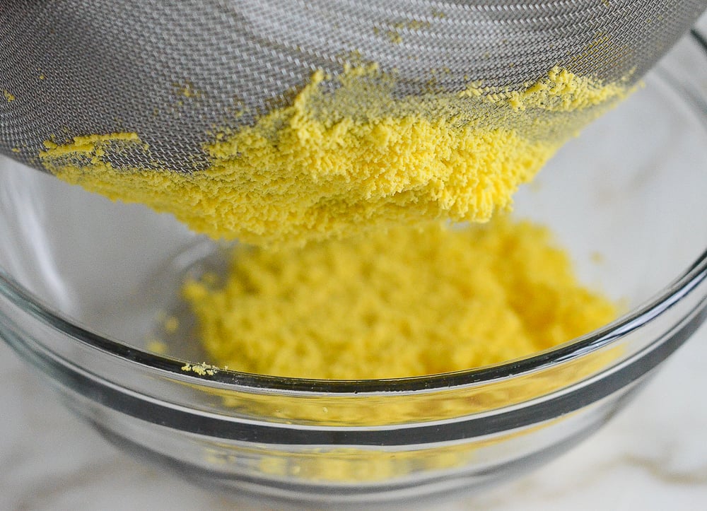 Cooked egg yolks coming through the bottom of a sieve.