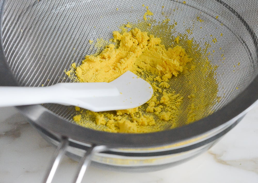 Spatula pushing cooked egg yolks through a sieve.