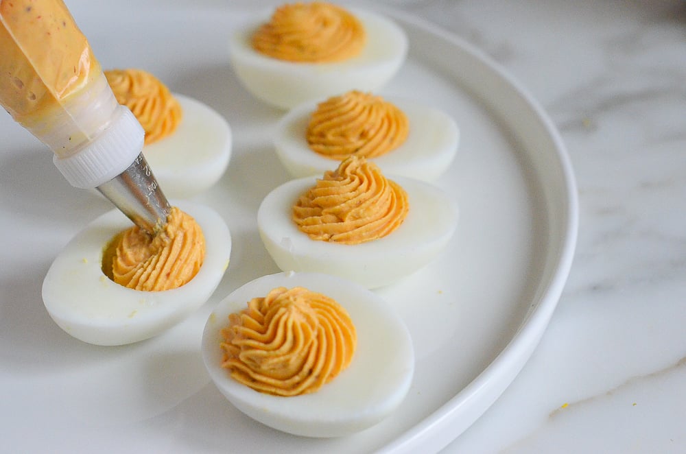 Piping bag piping egg yolk mixture into egg whites.