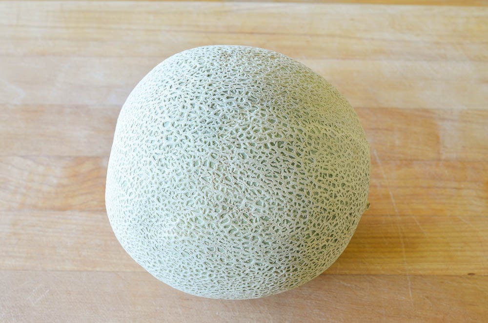 Whole cantaloupe on a wooden cutting board.