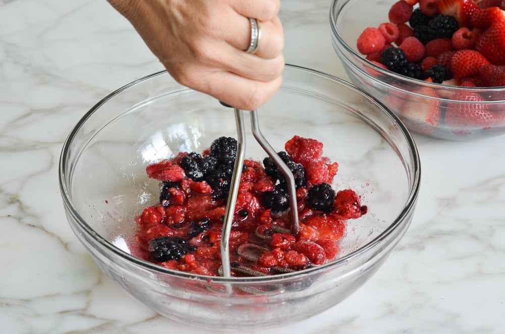 Person mashing berries with a potato masher.