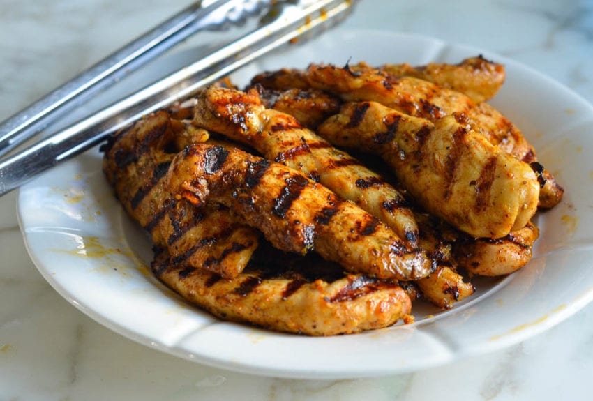 Grilled chicken on a plate with tongs.