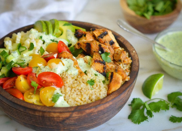 Wooden bowl of chicken and quinoa with toppings.