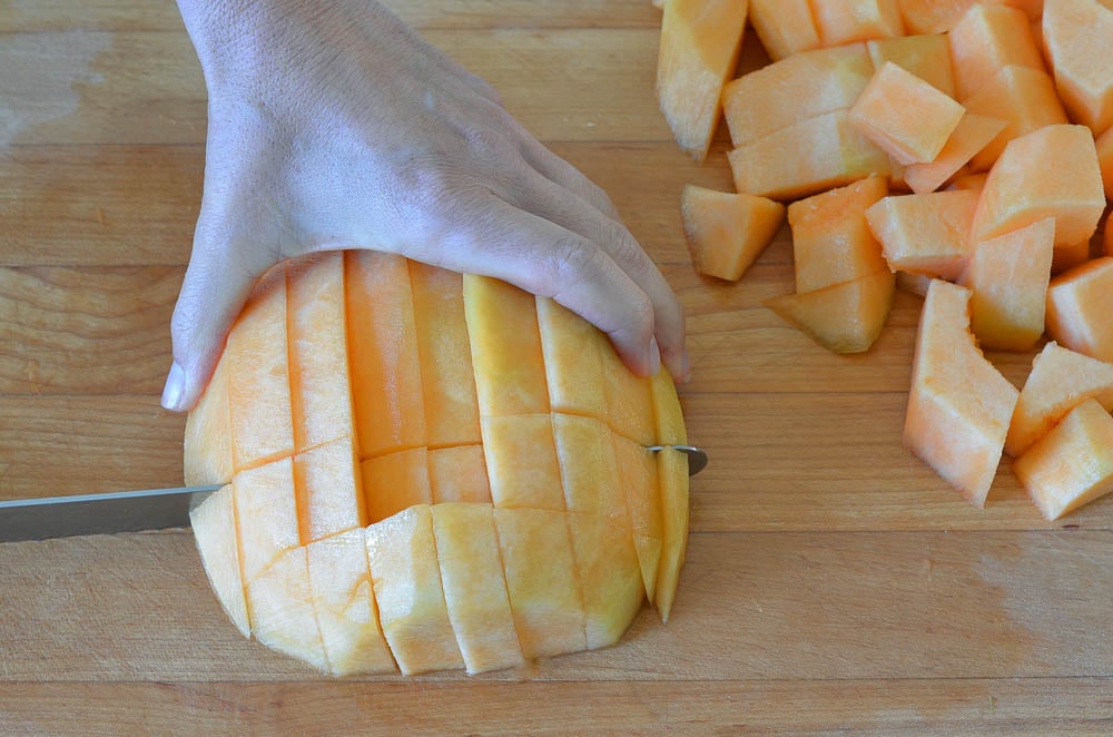 Person slicing a melon crosswise from previous cuts to create small pieces.