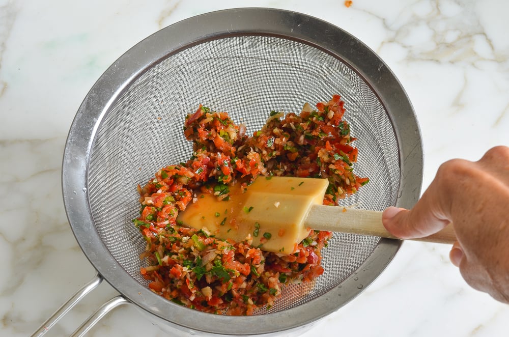 Spatula pressing processed vegetables in a sieve.