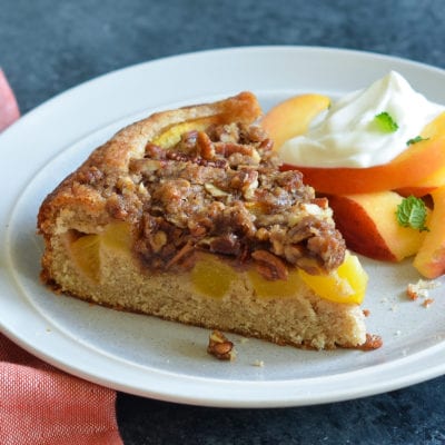 Slice of peach cake on a plate with peaches.