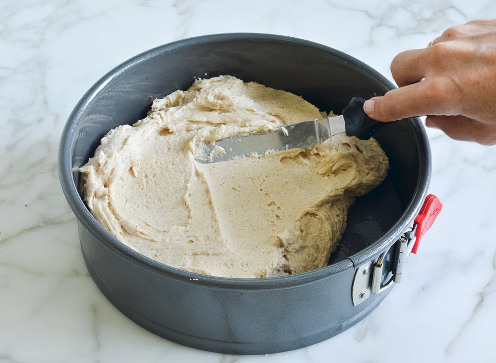 Person spreading cake batter in a springform pan.