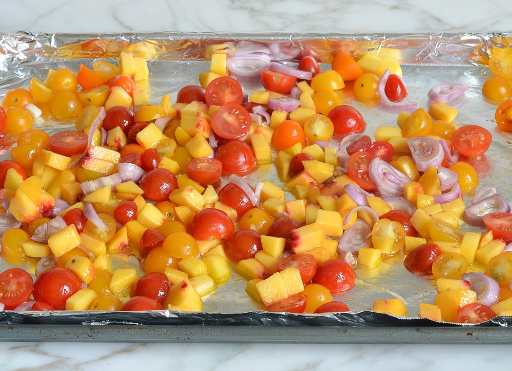 Tomatoes, peaches, and shallots on a lined baking sheet.