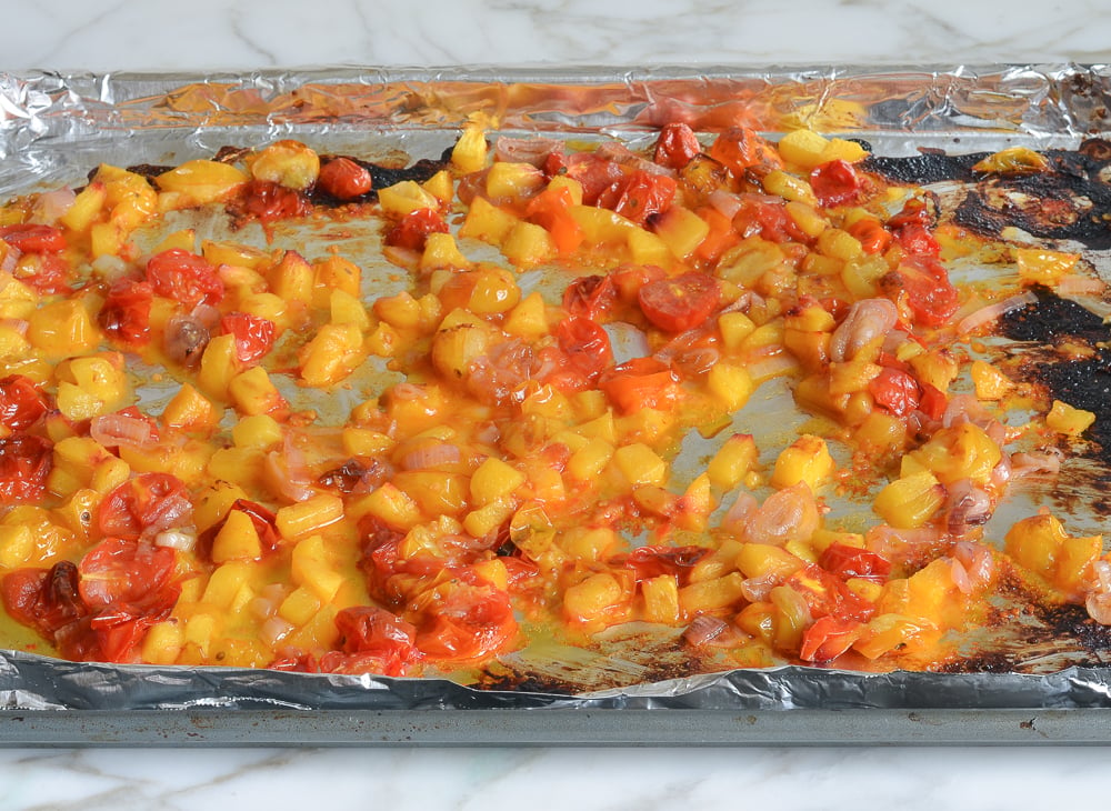 Roasted tomatoes, peaches, and shallots on a lined baking sheet.