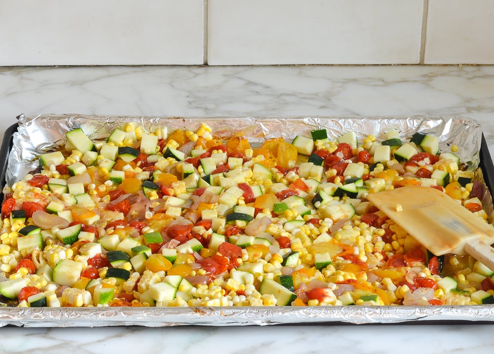 adding corn and zucchini to roasted tomatoes