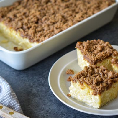 Slices of noodle kugel on a small plate next to a baking dish.