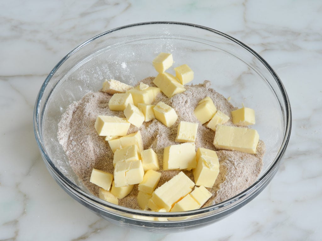 Pieces of butter over dry ingredients in a bowl.