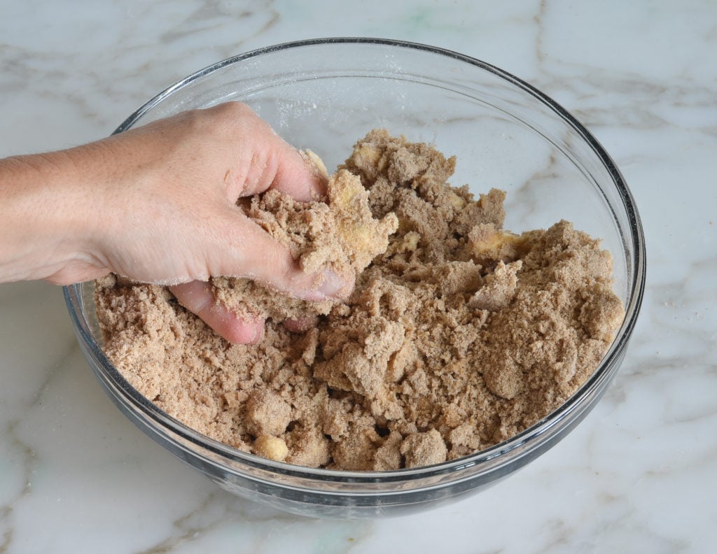 Person rubbing butter into dry ingredients.